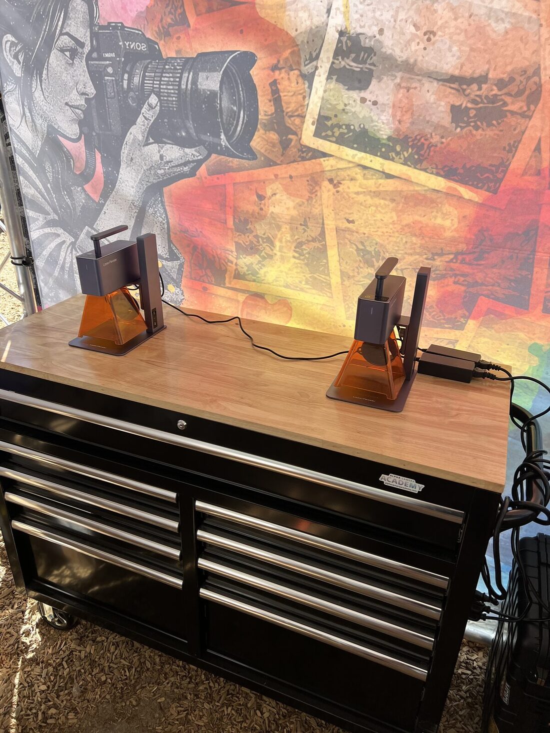 Two compact UV engravers customizing hard goods on a wood-top workstation at an event booth