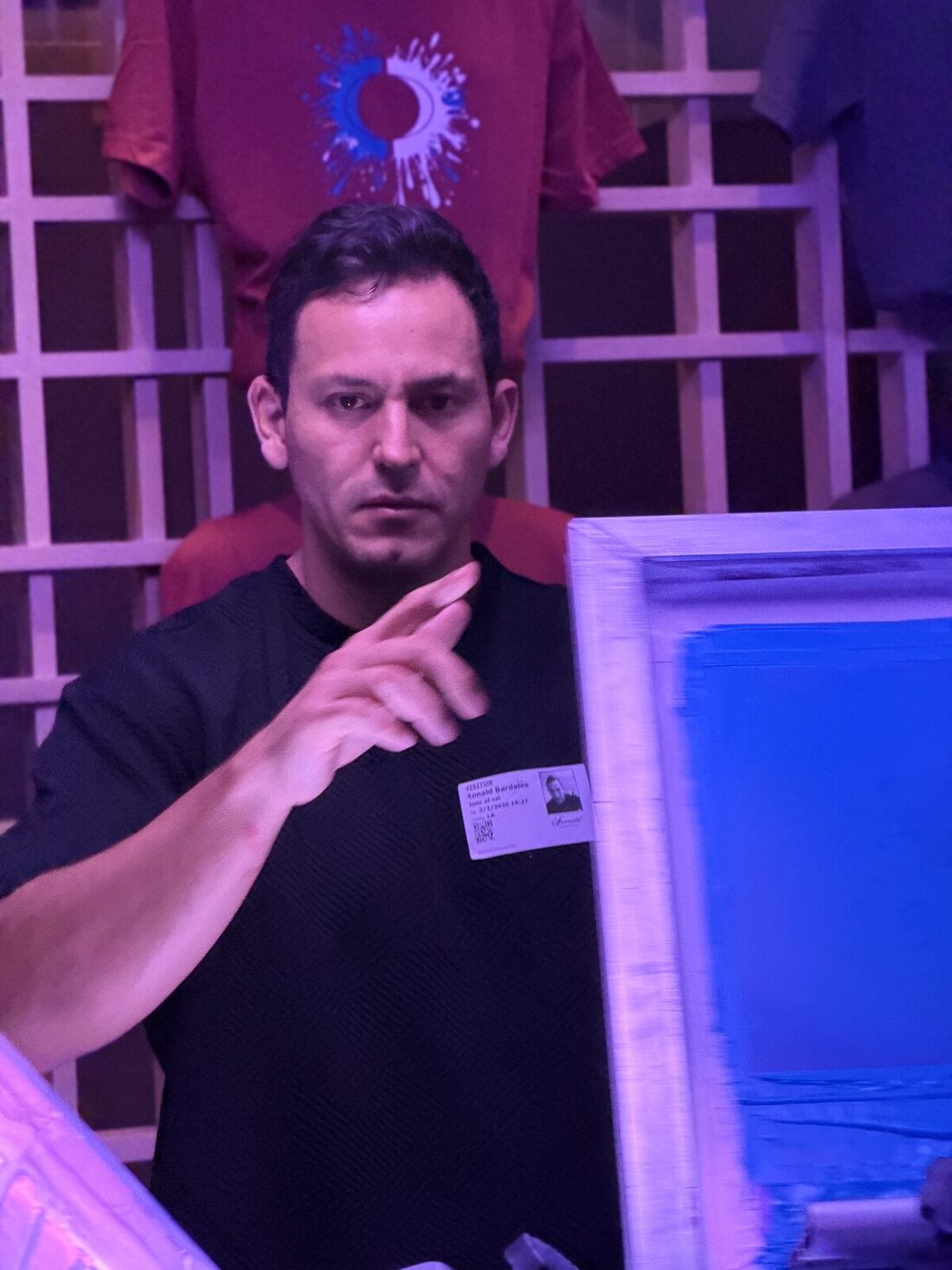 Merch Troop printer holding a screen loaded with blue ink in front of hanging printed tees
